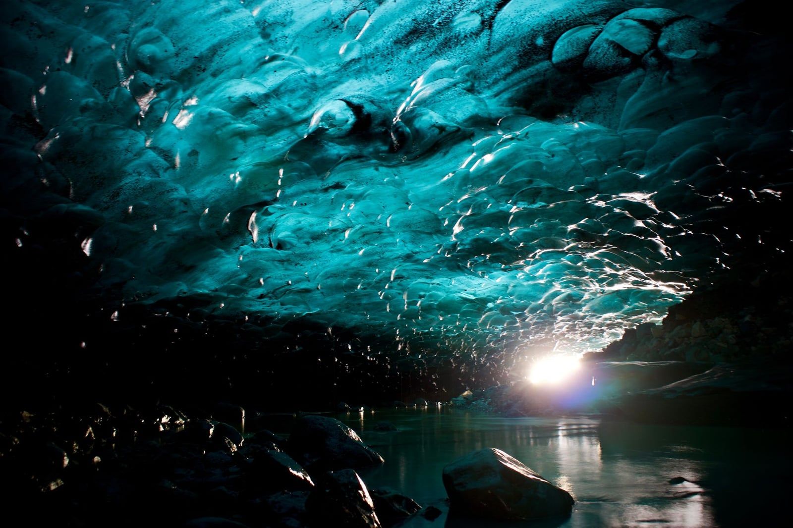 Sunlight illuminates the sculpted, luminous blue ceiling and reflective pool inside a glacier ice cave near Skaftafell.