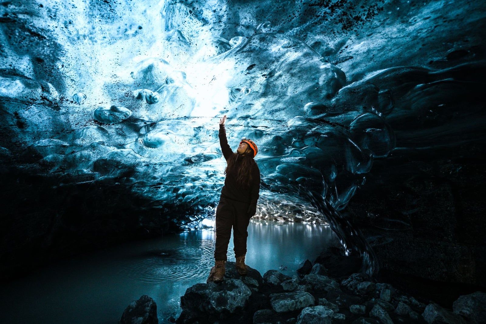 A visitor wearing a safety helmet stands inside a sculpted blue ice cave at Skaftafell Glacier in Iceland.