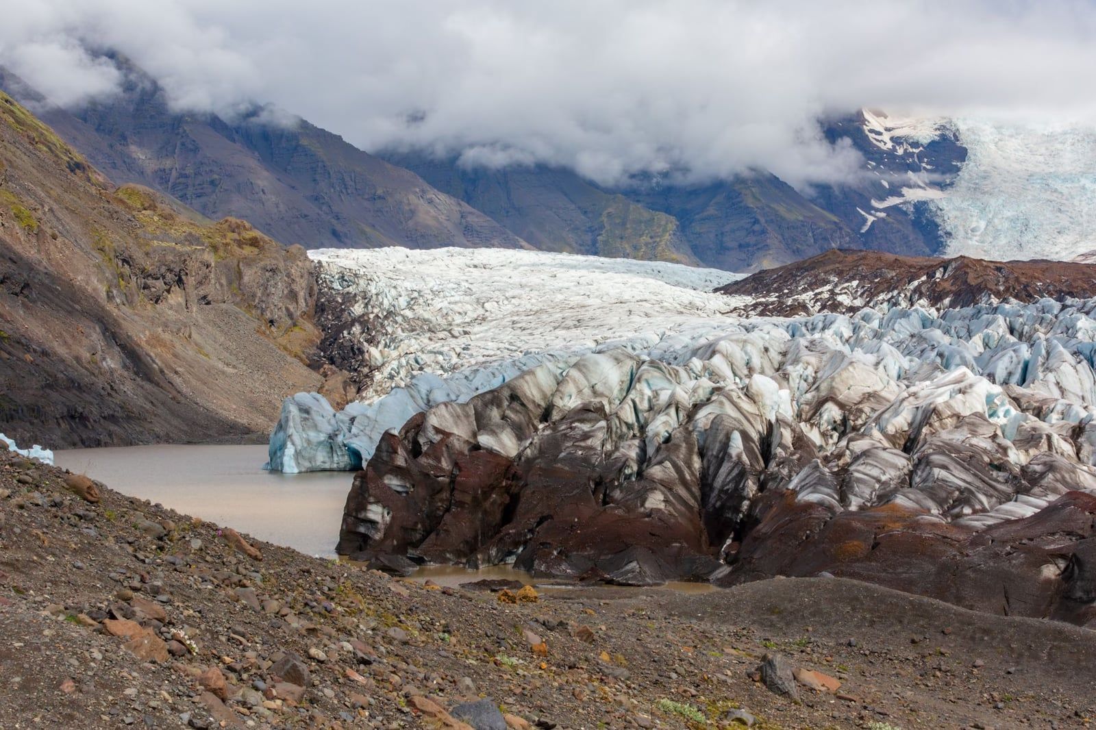 Zerklüftetes Eis des Svínafellsjökull-Gletschers fließt an steilen Bergkämmen vorbei auf eine Gletscherlagune nahe Skaftafell zu.