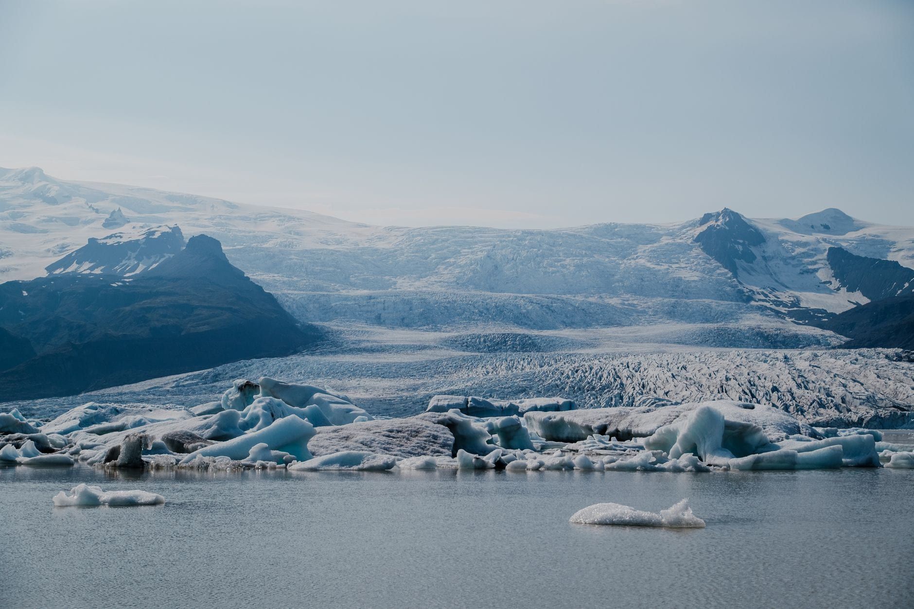 Icebergs flotan en una laguna glaciar frente a la amplia lengua del glaciar Skaftafell y crestas montañosas espolvoreadas de nieve.